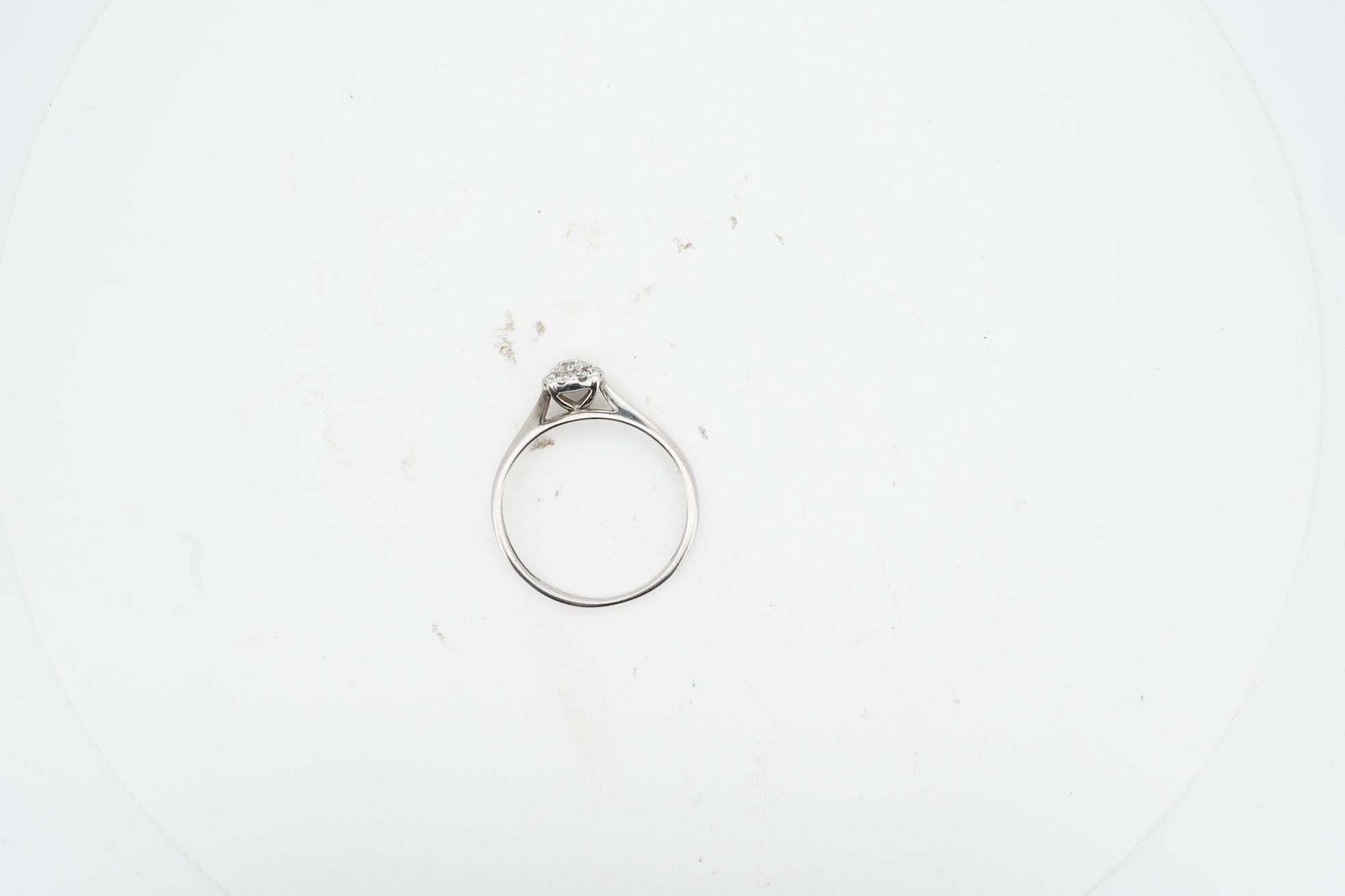 A diamond cluster ring, claw-set with a brilliant-cut diamond weighing approximately 0.10 carats, within a border of smaller brilliant-cut diamonds totalling approximately 0.09 carats, mounted in unmarked white metal, si